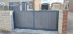 Flat top composite driveway gate with vertical composite boards and an aluminium frame installed between brick and stone pillars