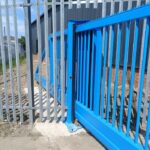 Metal vertical-bar sliding gate shown from the side at an industrial site entrance