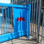 Metal vertical-bar sliding gate with branded panel installed at an industrial site entrance