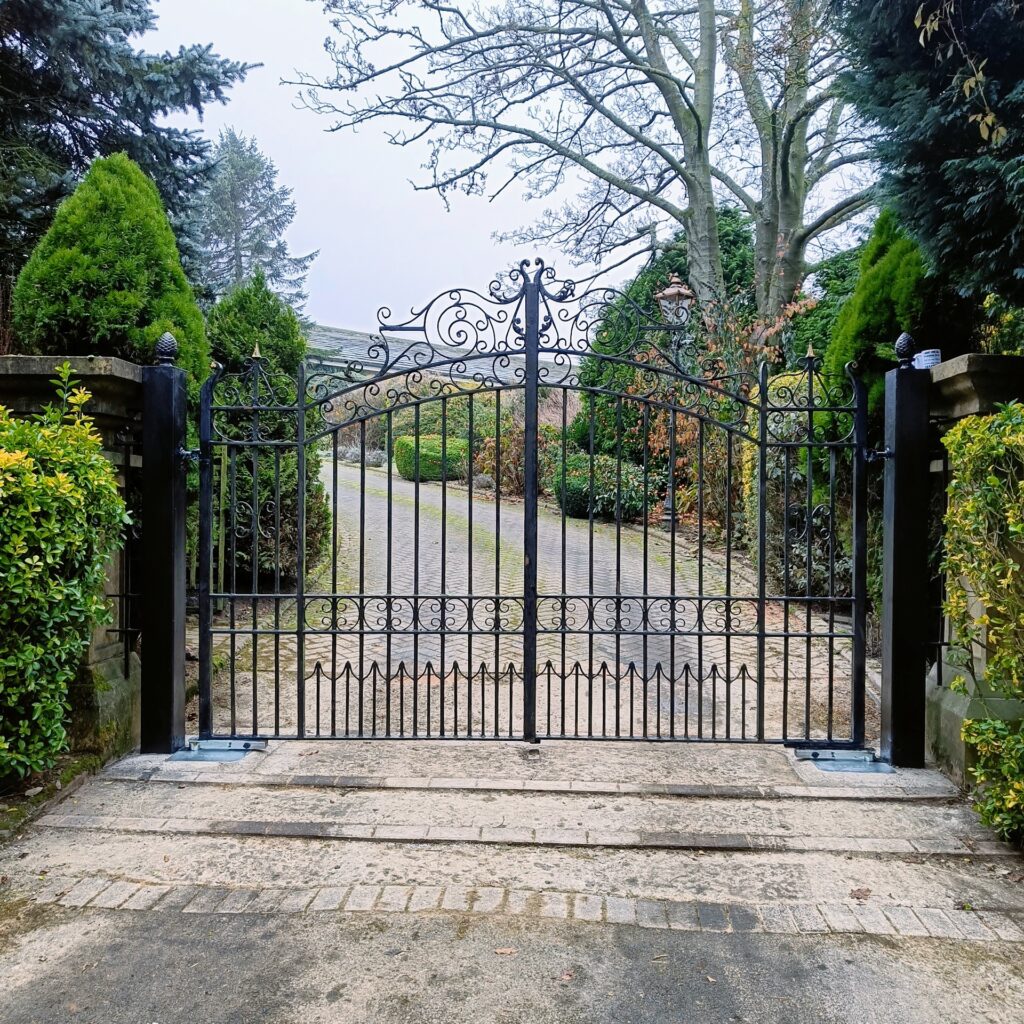 Black ornate metal gates at the entrance to a garden driveway - Leeds Electric Gates Black ornate metal gates at the entrance to a garden driveway